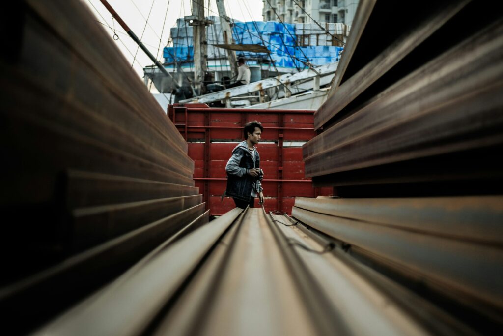 Man walking through an industrial area between steel beams in Jakarta's shipyard.