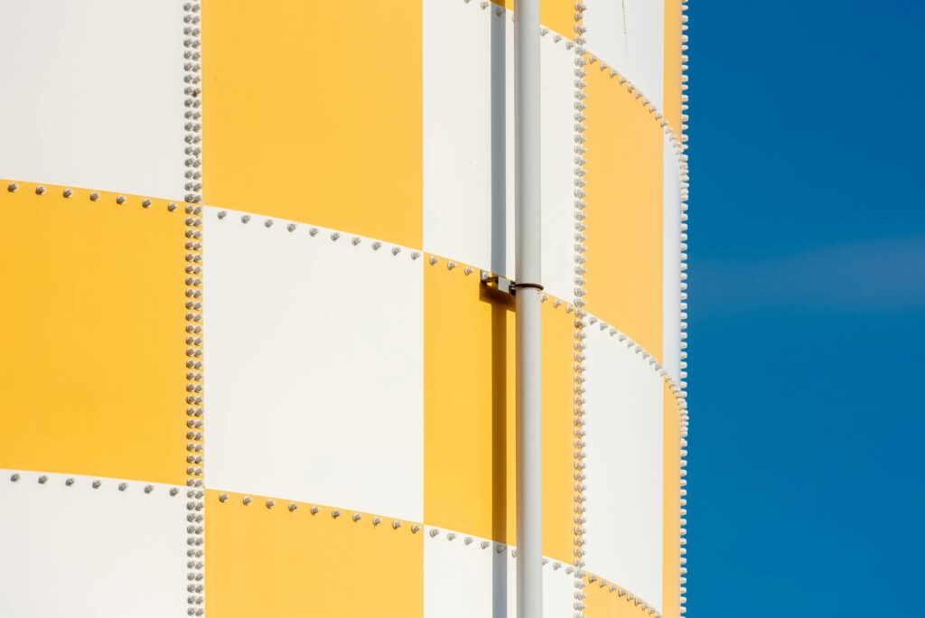 Close-up of a checkered yellow and white industrial tower with clear blue sky backdrop.