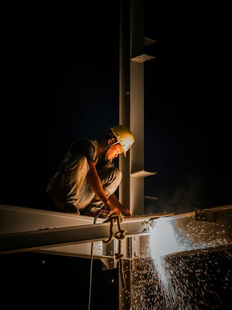 Industrial worker welding steel structure at night, casting bright sparks.